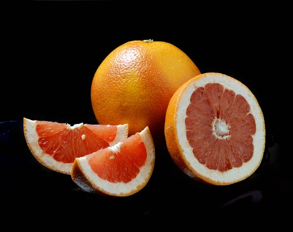 Grapefruit with slices on a black background — Stock Photo, Image