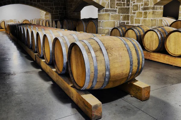 Wine barrels and metal cisterns in dark cellar — Stock Photo, Image