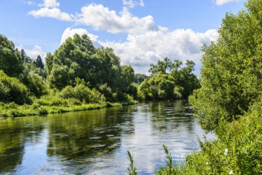 Mavi gökyüzü ve bulutlar nehrin yüzeyine yansıyor.