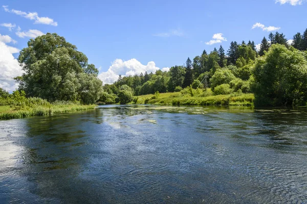 Mavi gökyüzü ve bulutlar nehrin yüzeyine yansıyor.