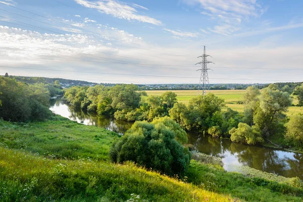 Arka planda yüksek voltaj kulesi olan nehir kıvrımının görüntüsü.