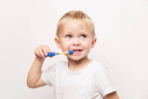 Little cute caucasian blond blue-eyed boy in a white t-shirt brushes his teeth on a white background Stock Image