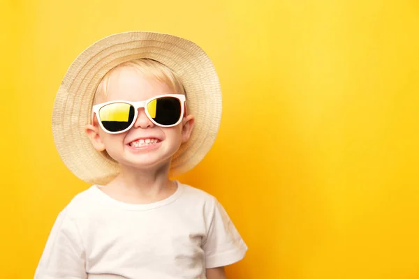 아기가 행복 한 얼굴로 웃으며 지푸라기 모자를 쓰고 노란 배경에 선글라스를 쓴 귀여운 금발의 남자 아이의 모습 이 카메라를 보고 있다. 원문을 위한 위치가 있는 카드 — 스톡 사진
