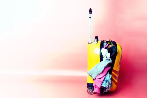 Kindergelber, nicht verschlossener Koffer mit Klebesachen und Kleidungsstücken auf rosa Hintergrund. Konzept Raser-Maut — Stockfoto