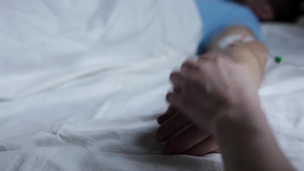 女人牵着他的手，在医院的病床上，男人和一个落水者牵手入睡。手部特写. — 图库视频影像