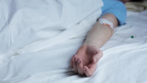 Чоловіча рука з дропером у медичній нічній сукні лежить на лікарняному ліжку і робить непристойний жест. — стокове відео