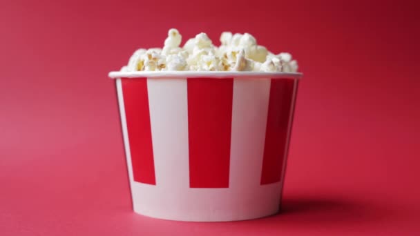 Hand nimmt Popcorn aus gestreifter und weißer Pappschachtel auf knallrotem Hintergrund — Stockvideo