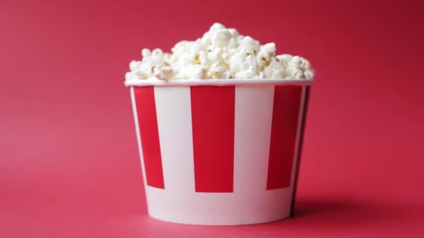 Hand taking popcorn from striped and white paper box on a bright red background — Stock Video