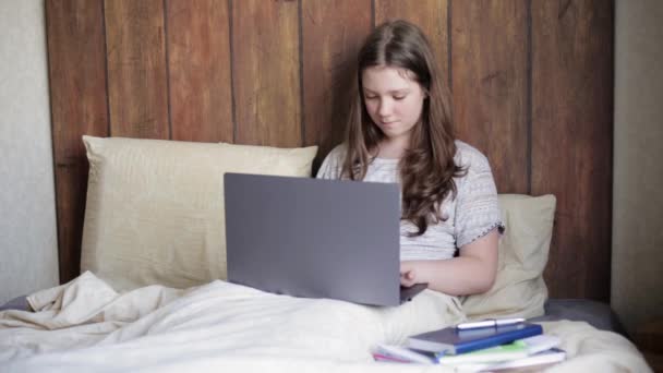 Девочка-подросток, использующая ноутбук для домашней работы в спальне. Дистанционное обучение онлайн — стоковое видео