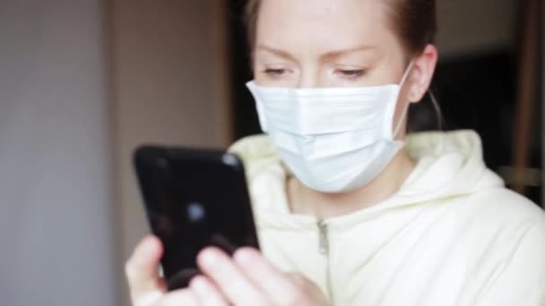 Jong blank meisje in een wegwerp medisch masker houdt een smartphone in haar hand. verontwaardigd, boos, nerveus door schokkend nieuws — Stockvideo