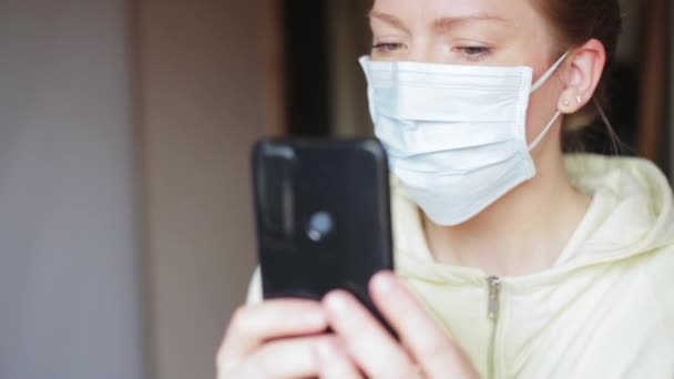 Jovem blogueira feminina leva selfie ou fazer videochamada em casa usando uma máscara médica protetora, covid 19 vírus pandemia mundo quarentena, perigo de gripe — Vídeo de Stock