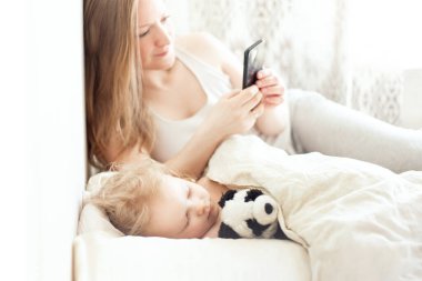Kız akıllı telefon kullanıyor Uyuyan bebeğin yanında 