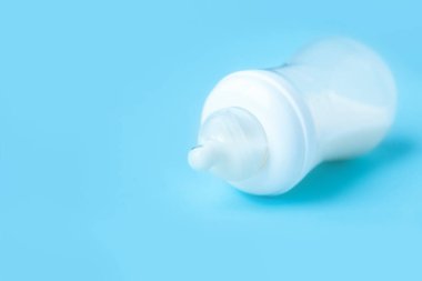 Fotokopi alanı olan saf mavi bir zemin üzerinde süt bulunan plastik bebek şişesi..