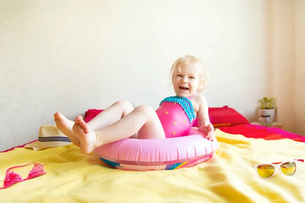 수영복을 입고 침대에 고무 반지를 달고 앉아 있는 소녀는 집에서 수영하는 것을 흉내낸다. — 스톡 사진
