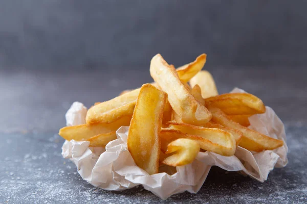 close up Potatoes fries in a little white paper bag on stone board with copy space