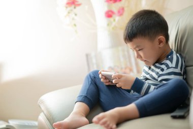 Covid-19 RMO (kısıtlı hareket emri) sırasında evde Asyalı çocuk (çocuk), akıllı telefonla oynuyor