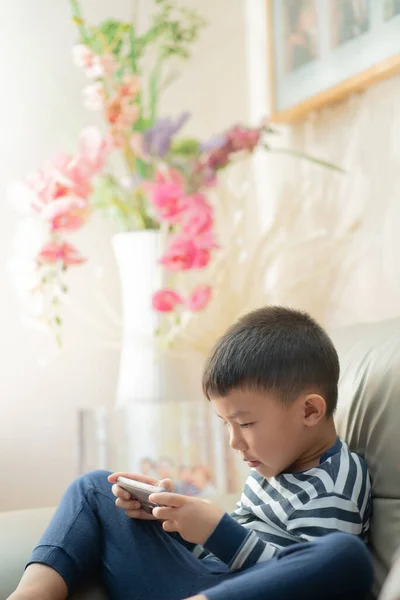 Asian child (boy) at home during Covid-19 RMO (restricted movement order) lockdown, playing with smartphone