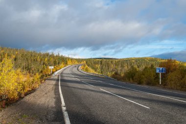 Kola otoyolu, Kola Yarımadası, Murmansk bölgesi. Kuzey köy yolu tepelerin arasında renkli sonbahar tundra ağaçları ile.