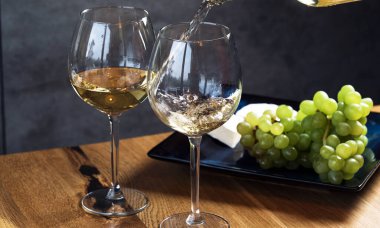 Ahşap masa zemininin üstündeki bardaklara beyaz şarap dökerek, üzüm ve peynirle hazırlanır. 