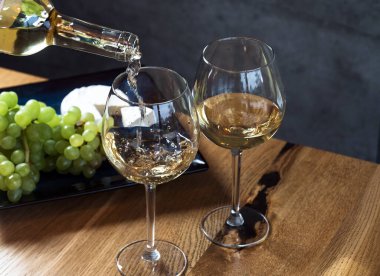 Ahşap masa zemininin üstündeki bardaklara beyaz şarap dökerek, üzüm ve peynirle hazırlanır. 