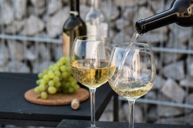 Kadehlere beyaz şarap dök, arka planda üzümler olsun.
