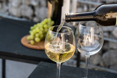 Kadehlere beyaz şarap dök, arka planda üzümler olsun.