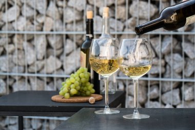 Kadehlere beyaz şarap dök, arka planda üzümler olsun.