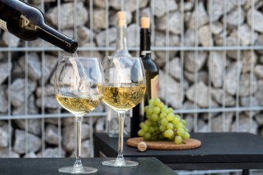 Kadehlere beyaz şarap dök, arka planda üzümler olsun.