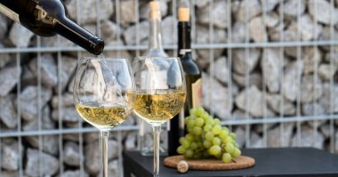 Kadehlere beyaz şarap dök, arka planda üzümler olsun.