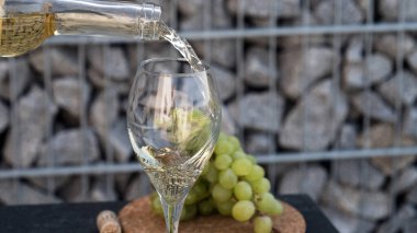 Beyaz şarabı bardağa dök, arka planda üzümler olsun.
