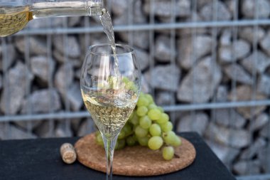 Beyaz şarabı bardağa dök, arka planda üzümler olsun.