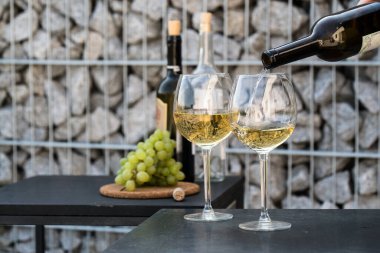 Kadehlere beyaz şarap dök, arka planda üzümler olsun.