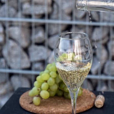 Beyaz şarabı bardağa dök, arka planda üzümler olsun.