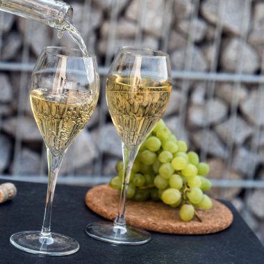 Kadehlere beyaz şarap dök, arka planda üzümler olsun.