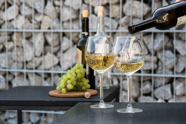 Kadehlere beyaz şarap dök, arka planda üzümler olsun.