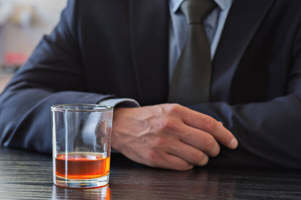Man in suit holding glass of Whiskey.