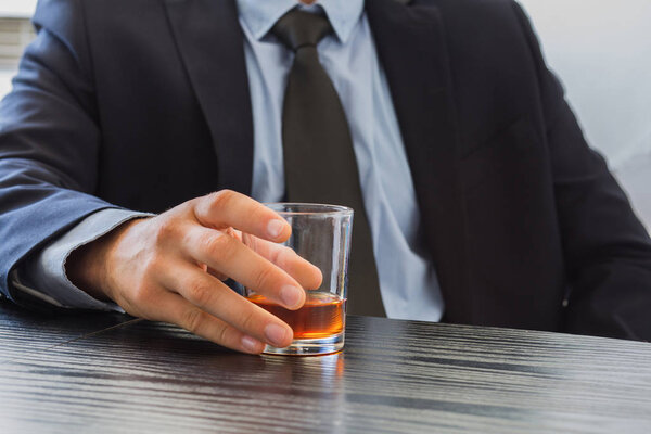 Man in suit holding glass of Whiskey.