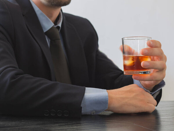 Man in suit holding glass of Whiskey.