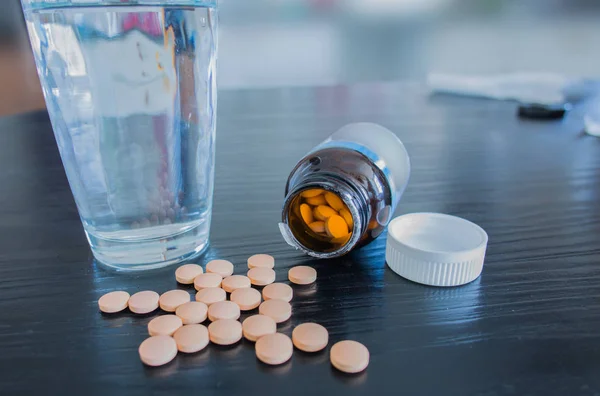 Open bottle with pills and glass of water