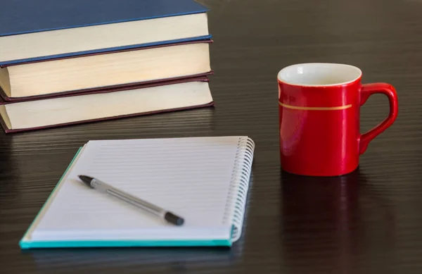 Pile of closed book with blank notebook and cup of coffee on wooden background.