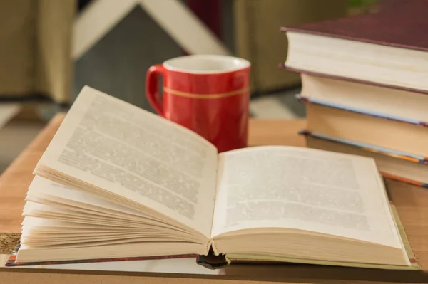 Pile of closed books and open book with cup of coffee