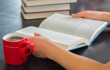 Yığın kapalı kitap ve kahve ev ile açık kitap tutan eller kadın..