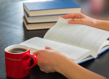 Yığın kapalı kitap ve kahve ev ile açık kitap tutan eller kadın..