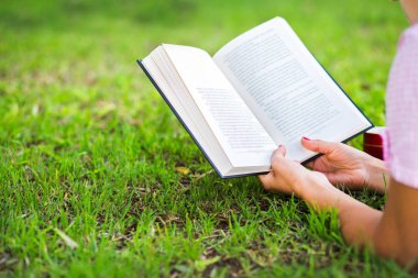 Kadın çimenlerin üzerinde açık bir kitap okuma