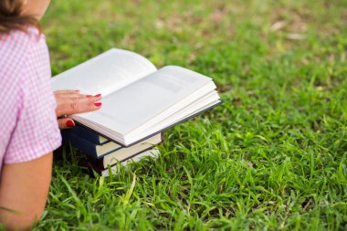 Kadın çimenlerin üzerinde açık bir kitap okuma
