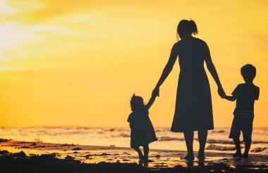 Anne ve iki çocuğu batımında sahilde yürüyüş