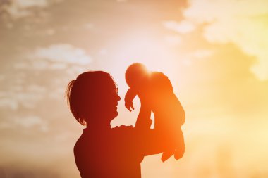 Baba ve küçük bebek günbatımında oynarken siluetleri