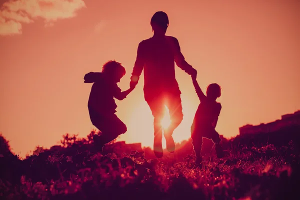 Happy family - father with son and daughter jumping from joy in sunset nature — Stockfoto