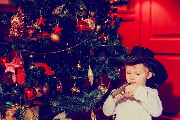 little boy in cowboy hat with gun at new year tree