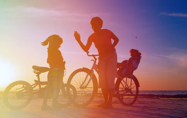 Mère heureuse avec deux enfants faisant du vélo au coucher du soleil — Photo